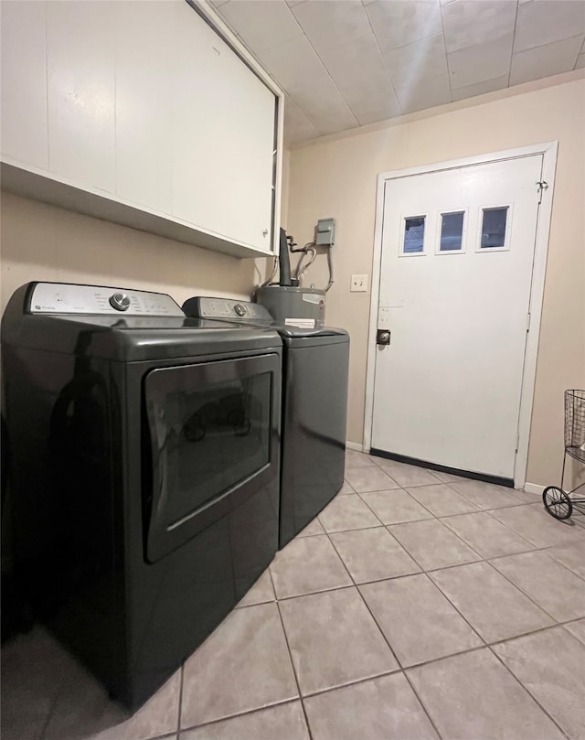 clothes washing area with light tile patterned flooring, cabinets, and washing machine and clothes dryer