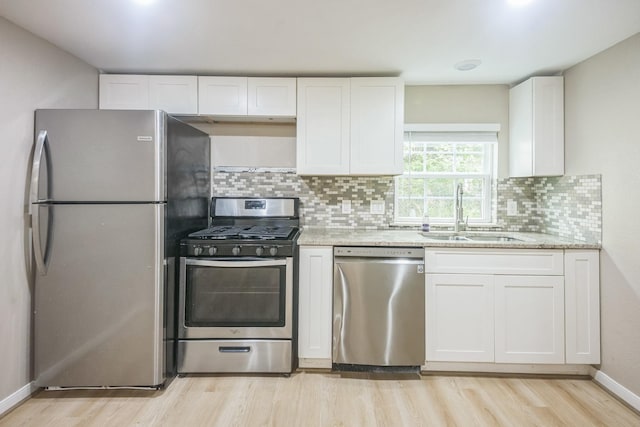 2409 Arbor St, Houston, TX 77004 - kitchen featuring appliances with stainless steel finishes, a sink, light wood-style floors, white cabinets, and decorative backsplash
