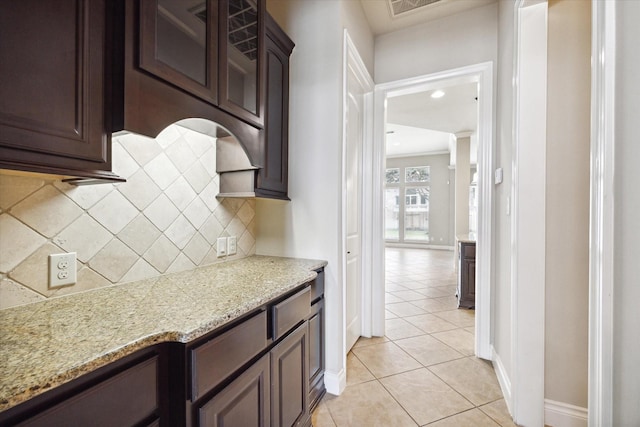 kitchen featuring backsplash, light stone counters, dark brown cabinets, and light tile patterned floors