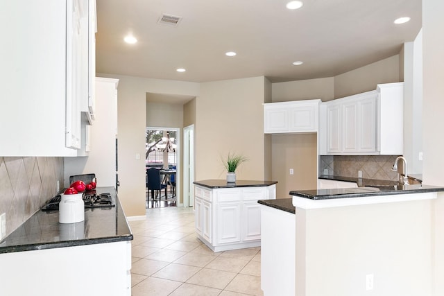 kitchen featuring stainless steel gas stovetop, white cabinetry, kitchen peninsula, and tasteful backsplash