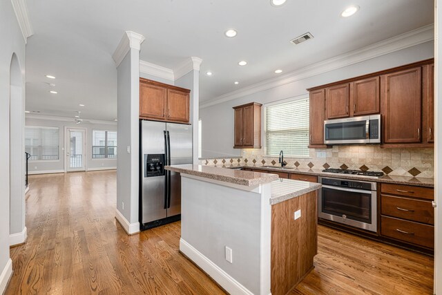 kitchen with light stone countertops, appliances with stainless steel finishes, tasteful backsplash, sink, and a center island