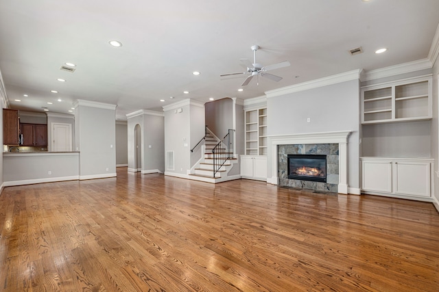 unfurnished living room with light wood-type flooring, built in shelves, ceiling fan, crown molding, and a tile fireplace