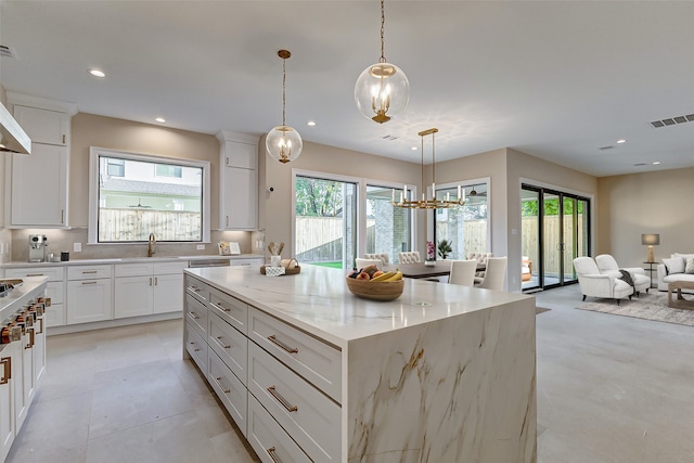 kitchen featuring a wealth of natural light, light stone counters, a kitchen island, and hanging light fixtures