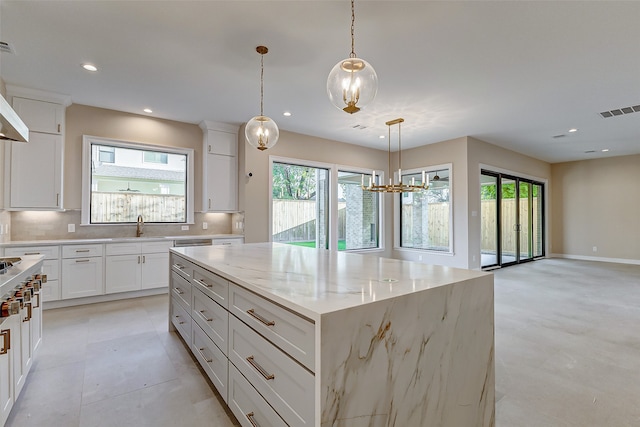 kitchen with pendant lighting, light stone counters, plenty of natural light, and a kitchen island