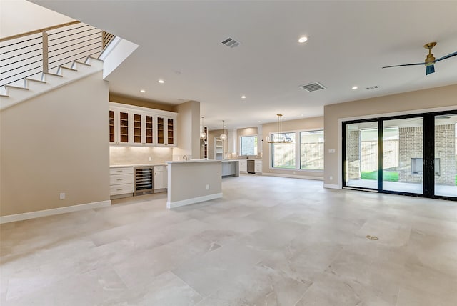 unfurnished living room with sink, ceiling fan with notable chandelier, and beverage cooler