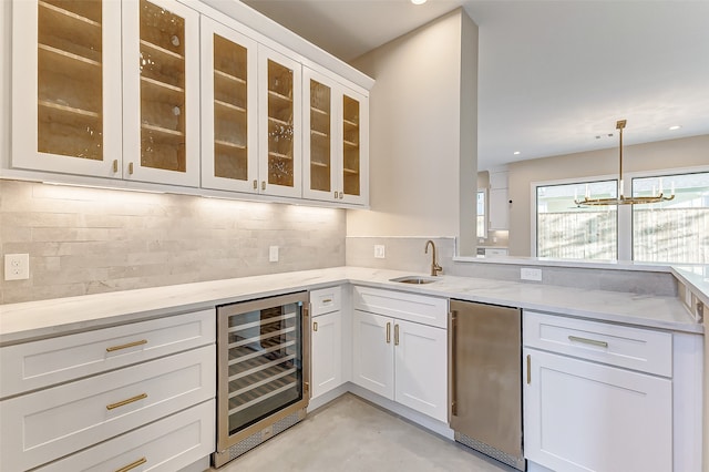 kitchen featuring sink, decorative light fixtures, an inviting chandelier, beverage cooler, and white cabinets