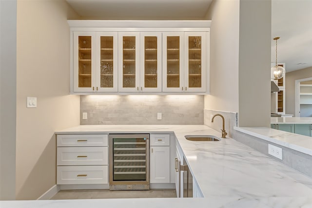 bar with white cabinets, tasteful backsplash, beverage cooler, light stone countertops, and sink