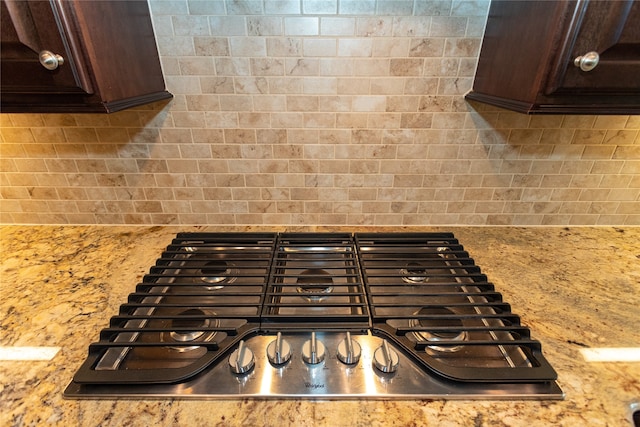 details with stainless steel gas stovetop, tasteful backsplash, light stone counters, and dark brown cabinets