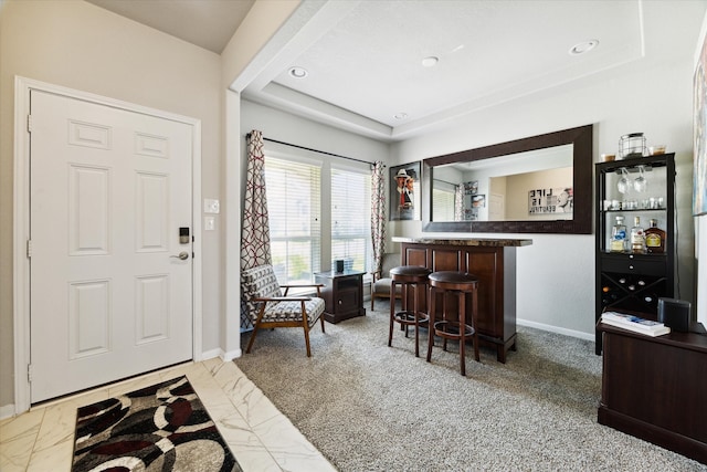 carpeted foyer entrance with a tray ceiling and indoor bar