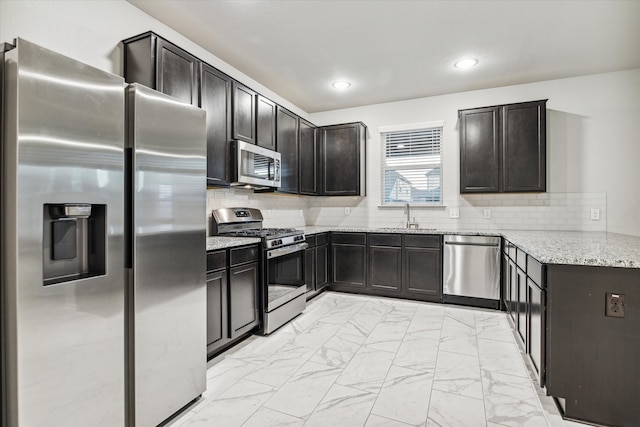 kitchen with backsplash, appliances with stainless steel finishes, sink, and light stone counters