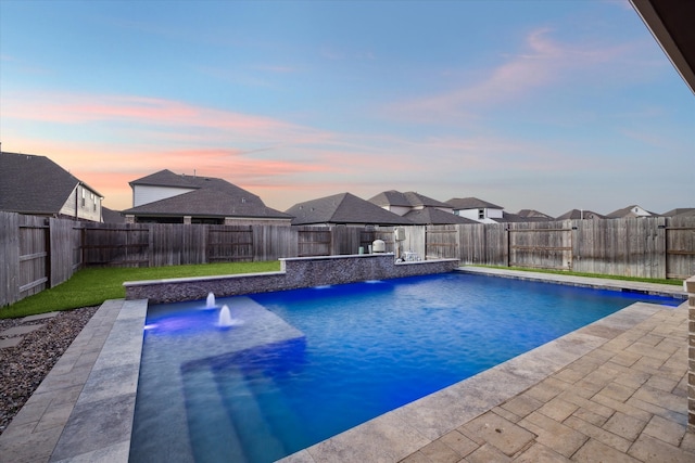 pool at dusk with a patio area, pool water feature, and a lawn