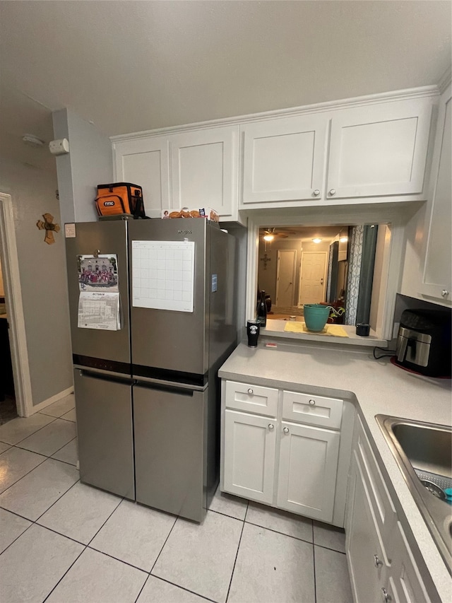 kitchen with light tile patterned floors, sink, stainless steel fridge, and white cabinets