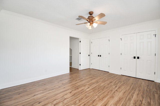 unfurnished bedroom featuring multiple closets, ceiling fan, ornamental molding, and hardwood / wood-style flooring