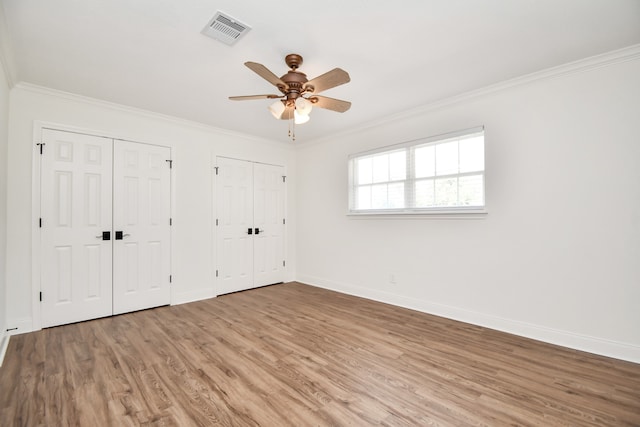 unfurnished bedroom featuring ceiling fan, hardwood / wood-style floors, two closets, and ornamental molding