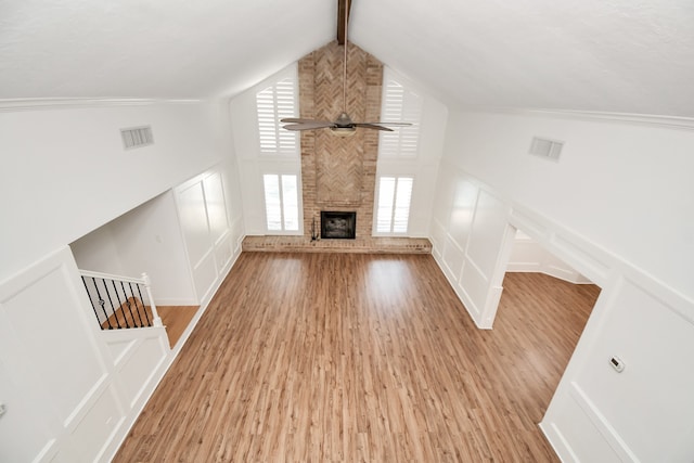 unfurnished living room with wood-type flooring, lofted ceiling with beams, a large fireplace, and ceiling fan