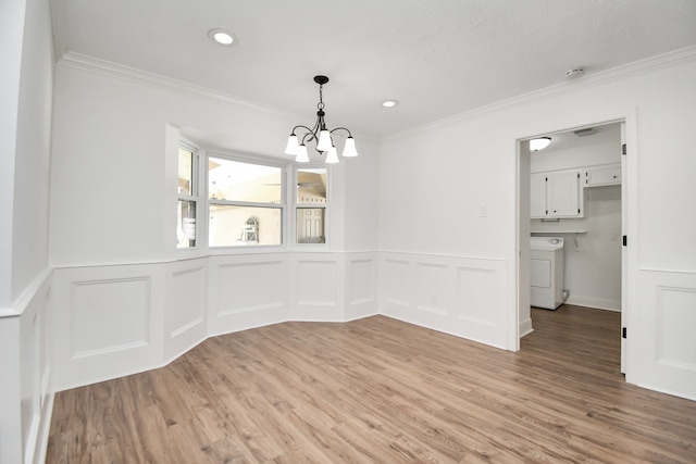 unfurnished dining area with a chandelier, washer / dryer, light hardwood / wood-style floors, and ornamental molding