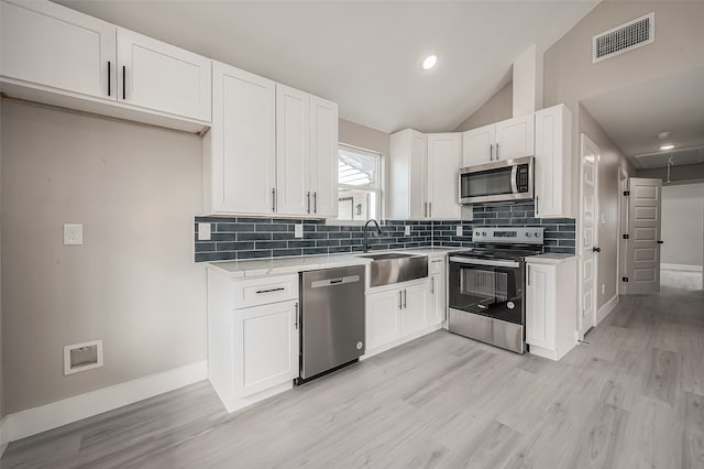 kitchen with stainless steel appliances, white cabinetry, sink, light hardwood / wood-style flooring, and vaulted ceiling