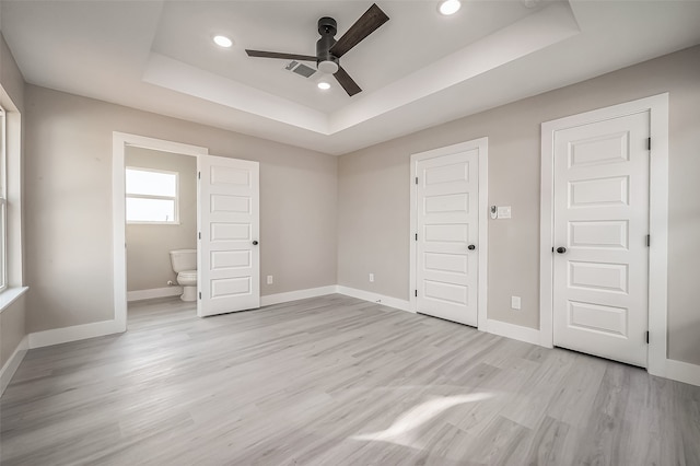 unfurnished bedroom featuring ceiling fan, connected bathroom, a raised ceiling, and light hardwood / wood-style flooring