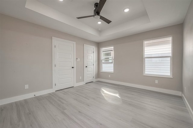 unfurnished bedroom featuring light hardwood / wood-style floors, ceiling fan, a raised ceiling, and multiple closets