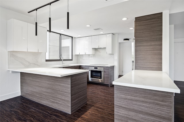 kitchen featuring oven, kitchen peninsula, white cabinetry, dark wood-type flooring, and decorative light fixtures