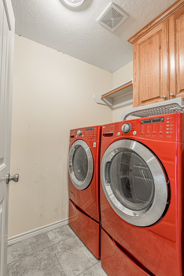 clothes washing area with cabinets, a textured ceiling, and separate washer and dryer