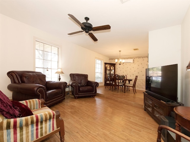 living room featuring a wall unit AC, ceiling fan with notable chandelier, light wood-type flooring, and plenty of natural light