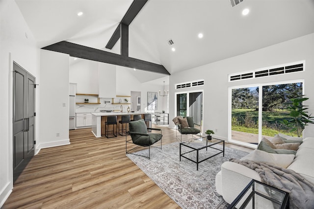 living room with high vaulted ceiling, an inviting chandelier, sink, light hardwood / wood-style flooring, and beam ceiling