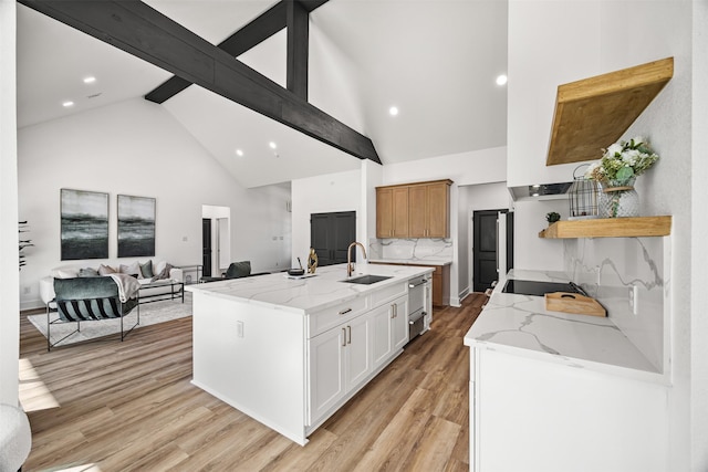 kitchen featuring white cabinetry, sink, light stone countertops, light hardwood / wood-style flooring, and a kitchen island with sink