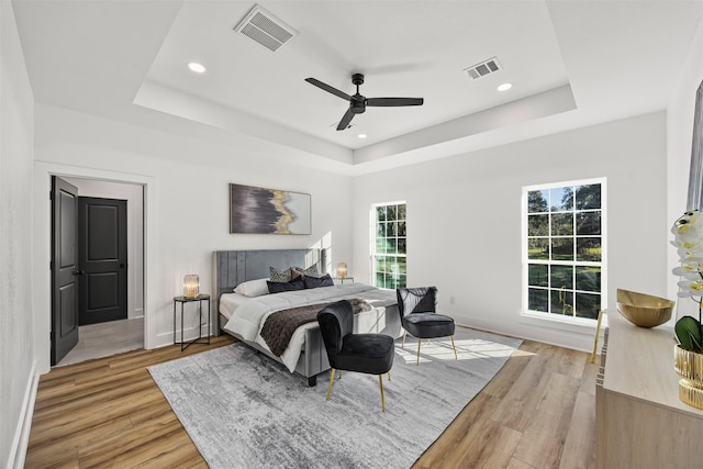 bedroom featuring light hardwood / wood-style flooring, a raised ceiling, and ceiling fan