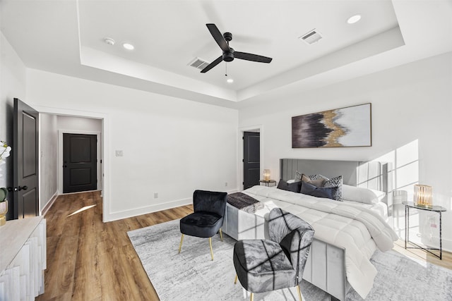 bedroom featuring a raised ceiling, ceiling fan, and wood-type flooring