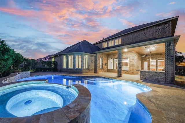 pool at dusk featuring a patio area and an in ground hot tub