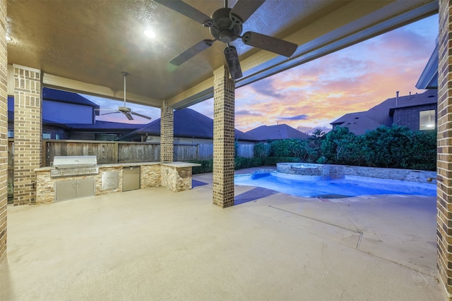 patio terrace at dusk with ceiling fan, a jacuzzi, grilling area, and an outdoor kitchen