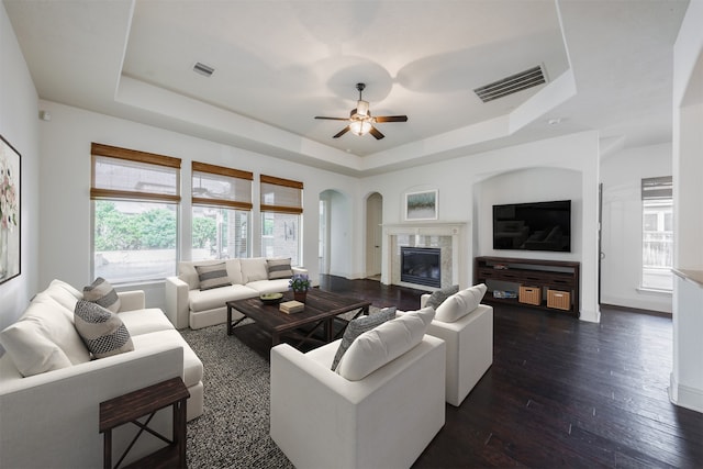 living room with a high end fireplace, dark hardwood / wood-style floors, a raised ceiling, and ceiling fan