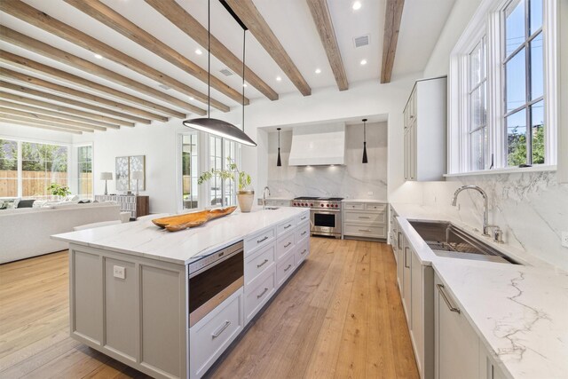 kitchen with sink, a center island with sink, custom range hood, and decorative light fixtures