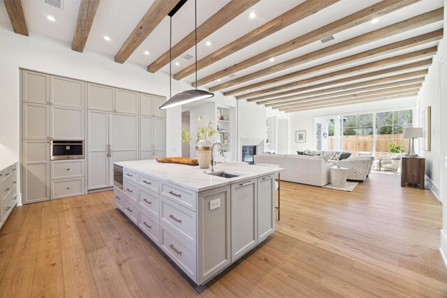 kitchen featuring a center island with sink, beamed ceiling, light stone countertops, sink, and decorative light fixtures