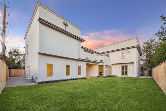 back house at dusk featuring a patio area and a lawn