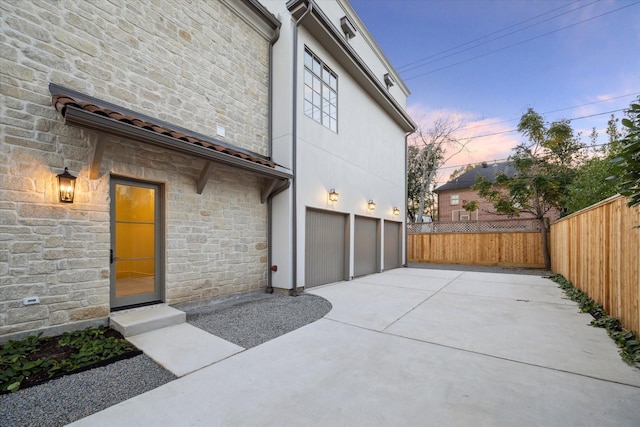 exterior space featuring concrete driveway, stone siding, an attached garage, and fence