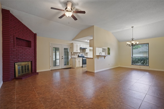 unfurnished living room featuring dark tile patterned floors, vaulted ceiling, a brick fireplace, a textured ceiling, and ceiling fan with notable chandelier