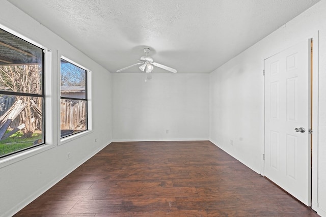 empty room featuring ceiling fan, a healthy amount of sunlight, a textured ceiling, and dark hardwood / wood-style flooring