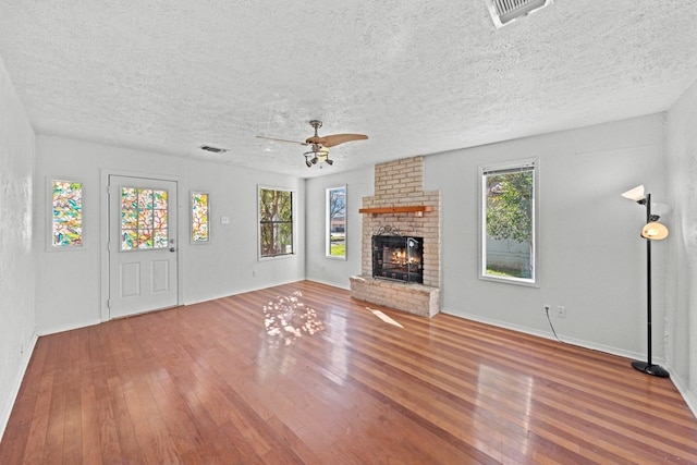 unfurnished living room featuring a textured ceiling, wood-type flooring, a wealth of natural light, and a brick fireplace