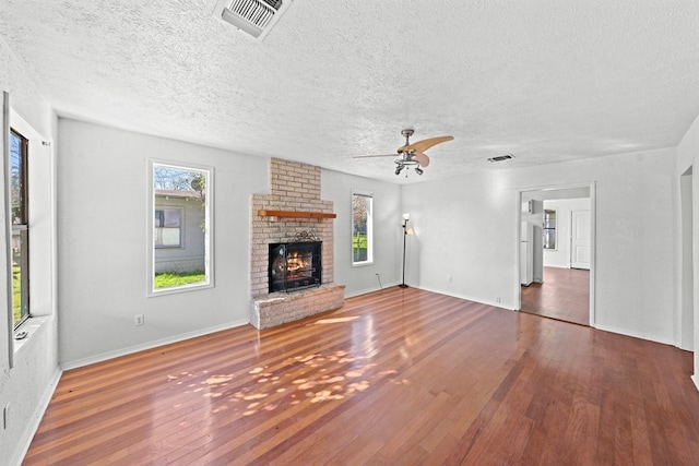 unfurnished living room with a textured ceiling, dark hardwood / wood-style flooring, a wealth of natural light, and a brick fireplace