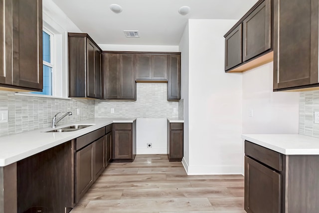 kitchen with dark brown cabinets, light hardwood / wood-style flooring, sink, and tasteful backsplash