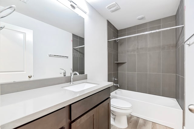 full bathroom with hardwood / wood-style floors, vanity, tiled shower / bath combo, and toilet