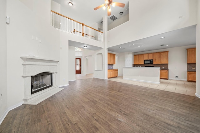 unfurnished living room featuring ceiling fan, a high ceiling, and light wood-type flooring