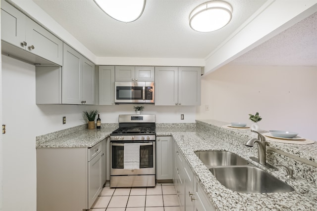 kitchen featuring stainless steel appliances, sink, light stone countertops, light tile patterned floors, and a textured ceiling