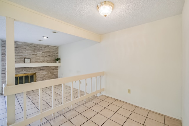 spare room with a textured ceiling, beamed ceiling, a fireplace, and light tile patterned floors