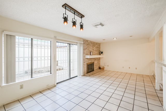 unfurnished living room with light tile patterned flooring, a textured ceiling, a brick fireplace, and plenty of natural light