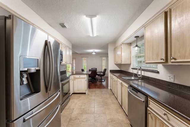 kitchen featuring hanging light fixtures, kitchen peninsula, light brown cabinetry, appliances with stainless steel finishes, and a textured ceiling