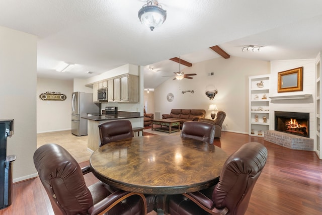 dining room featuring lofted ceiling with beams, a textured ceiling, a brick fireplace, light hardwood / wood-style floors, and ceiling fan