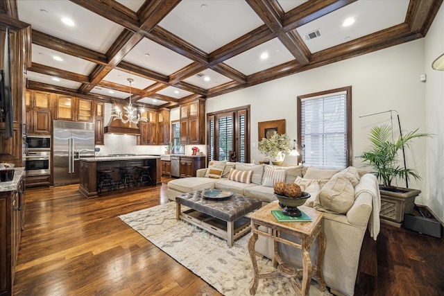 living room with dark wood-type flooring, beamed ceiling, an inviting chandelier, and coffered ceiling